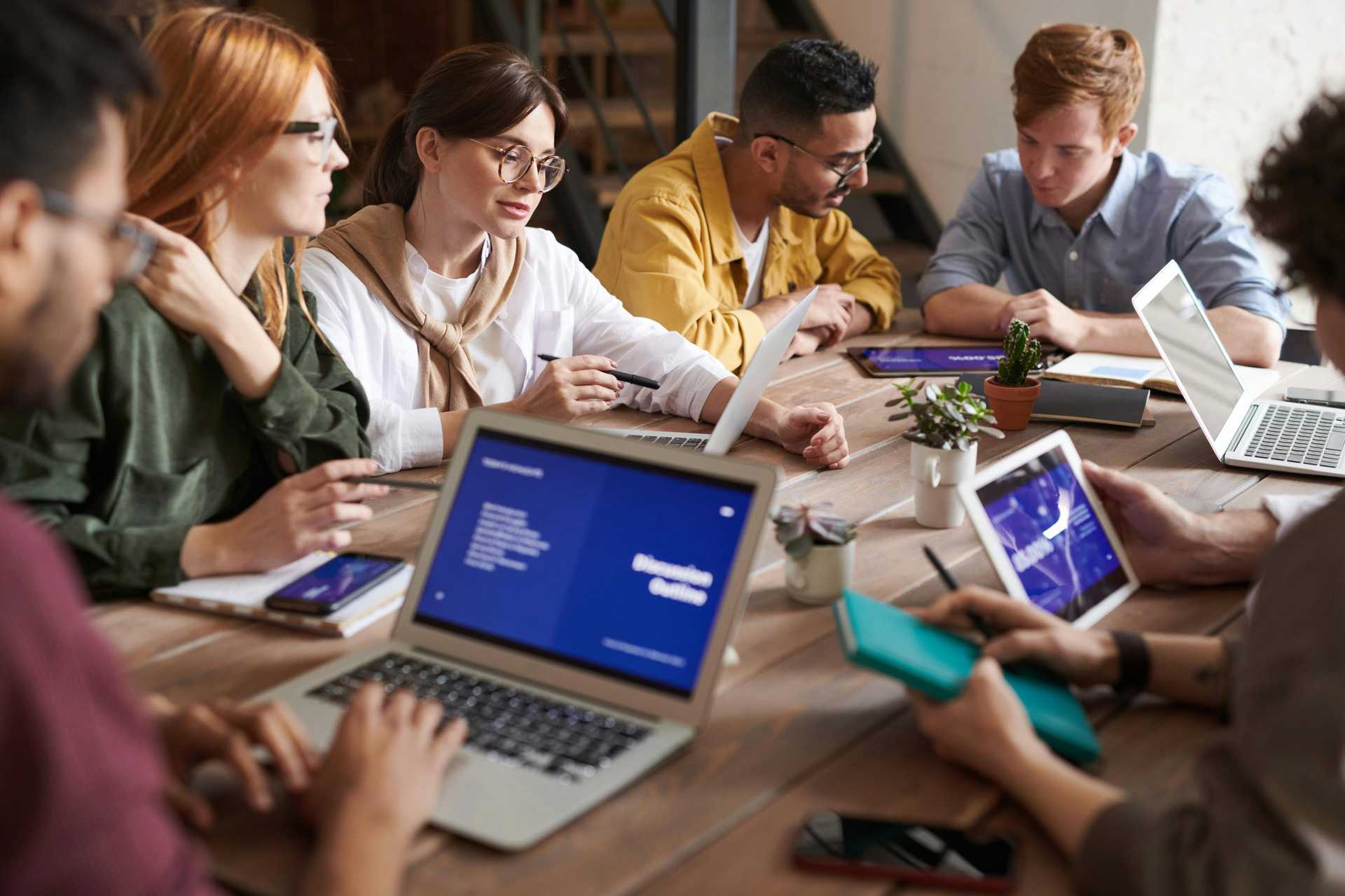 A group of people collobrate on a desk, they're using laptops and working on a technology project which could be an IoT project or some Enterprise project.